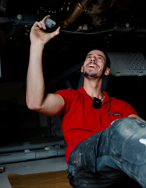 Homme souriant sous une voiture, éclairant le carter moteur
